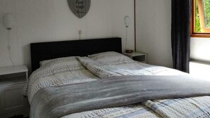 Un dormitorio con cama, una mesita de noche, luz empotrada en la pared, decoración con forma de corazón y ventana con cortinas.