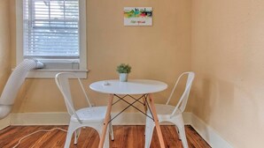 A small room with a white table and two white chairs, a potted plant, and a window with blinds. - Craftsman Guest Suite | Heart of Cooper-Young (Memphis)