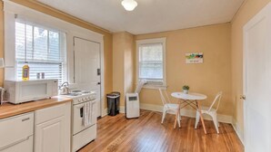 A compact kitchen with a stove, microwave, and sink, wooden flooring, and a small dining table with chairs. - Craftsman Guest Suite | Heart of Cooper-Young (Memphis)