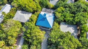 An aerial view of a residential area with a house featuring a blue roof, surrounded by lush greenery and other houses. - Dream home with incredible outdoor space. Walk to beach & restaurants! (Sanibel)