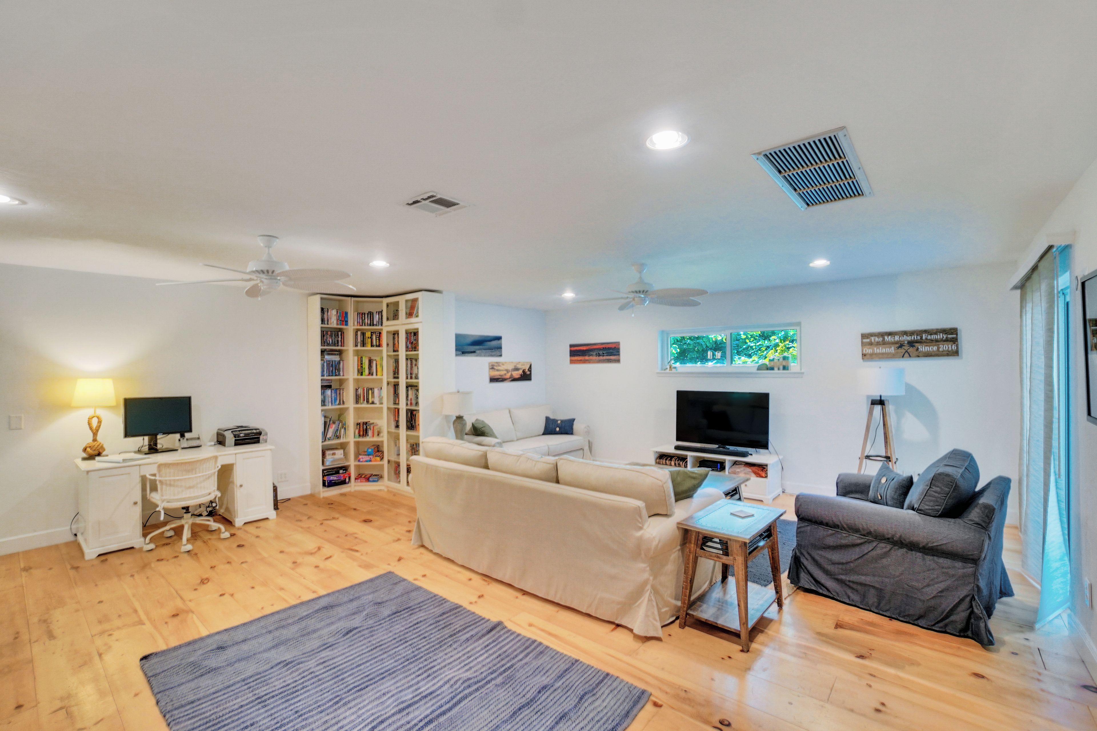 A living room with a sofa, a coffee table, a television, a bookshelf, and a desk with a computer.