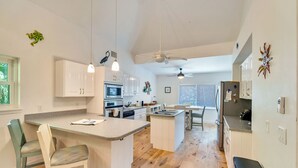 A modern kitchen with white cabinets, a central island, and a dining area with chairs. - Dream home with incredible outdoor space. Walk to beach & restaurants! (Sanibel)
