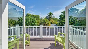 A deck with a white railing, two green chairs, and a view of lush greenery and palm trees. - Dream home with incredible outdoor space. Walk to beach & restaurants! (Sanibel)