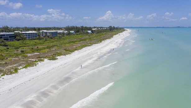 A beach with a clear view of the ocean, a few boats, and buildings in the background. - Dream home with incredible outdoor space. Walk to beach & restaurants! (Sanibel)