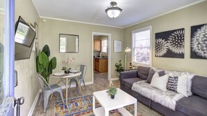 Una sala de estar con un sofá gris, una mesa de centro, una mesa de comedor con sillas y una cocina visible a través de un arco.