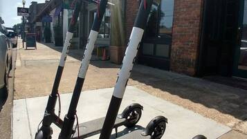 A row of electric scooters parked on a sidewalk in front of a building with the number 2087.