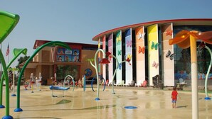 Zona de juegos acuáticos al aire libre con estructuras de juego coloridas y un edificio decorado con mariposas al fondo.