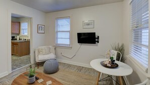 Una sala de estar moderna con una televisión de pantalla plana montada en la pared, una mesa de centro redonda, un sillón blanco y una mesita auxiliar con objetos decorativos.