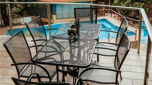 Un área junto a la piscina con barandilla de cristal, una estructura de techo rojo y una alberca.