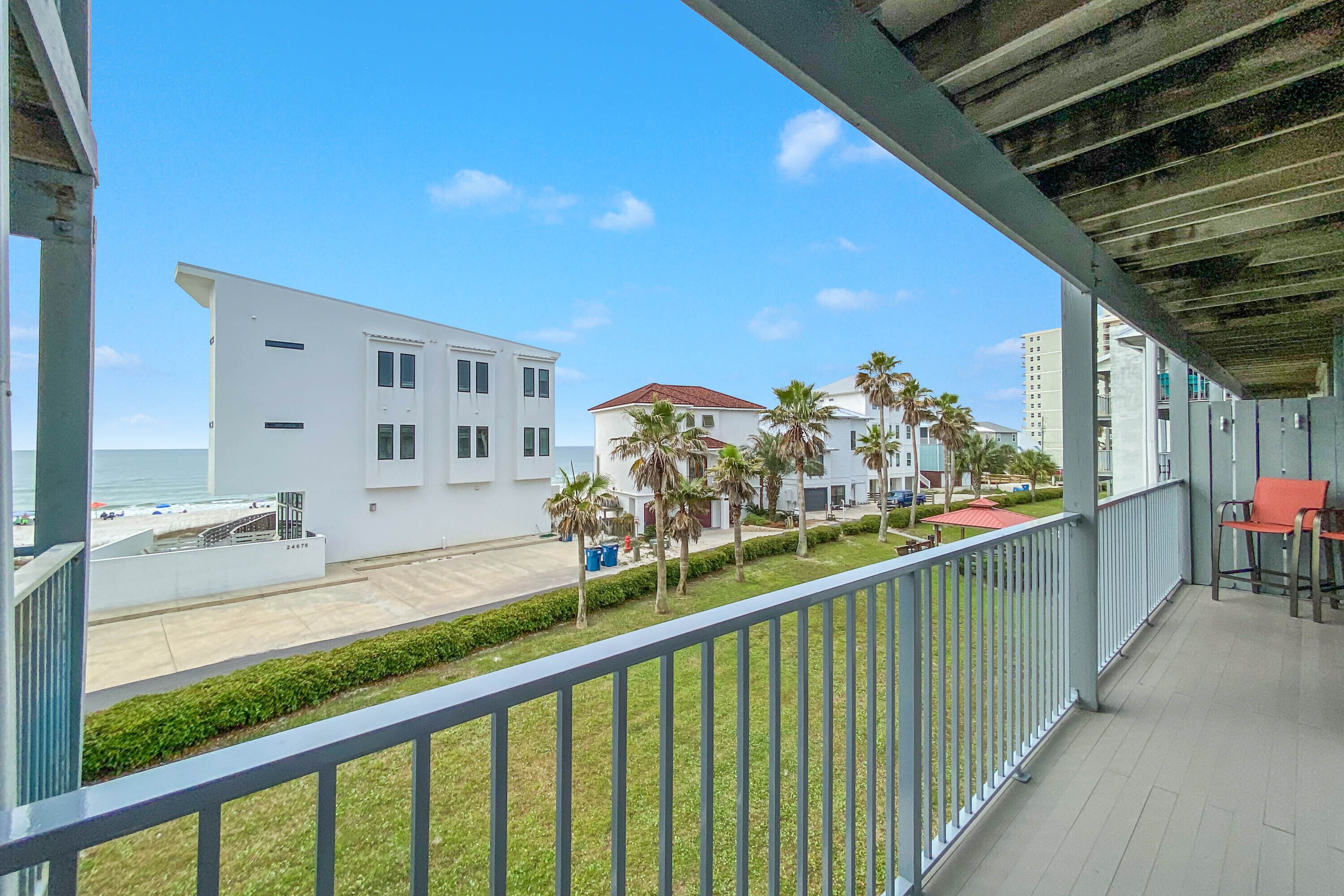 A balcony with a view of a beach, palm trees, and a white building.