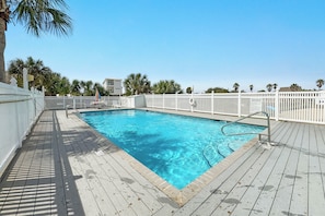 A swimming pool with a wooden deck, white fence, and palm trees in the background. - Seascape 210- CONVENIENT LOCATION, FUN FOR THE WHOLE FAMILY (Orange Beach)