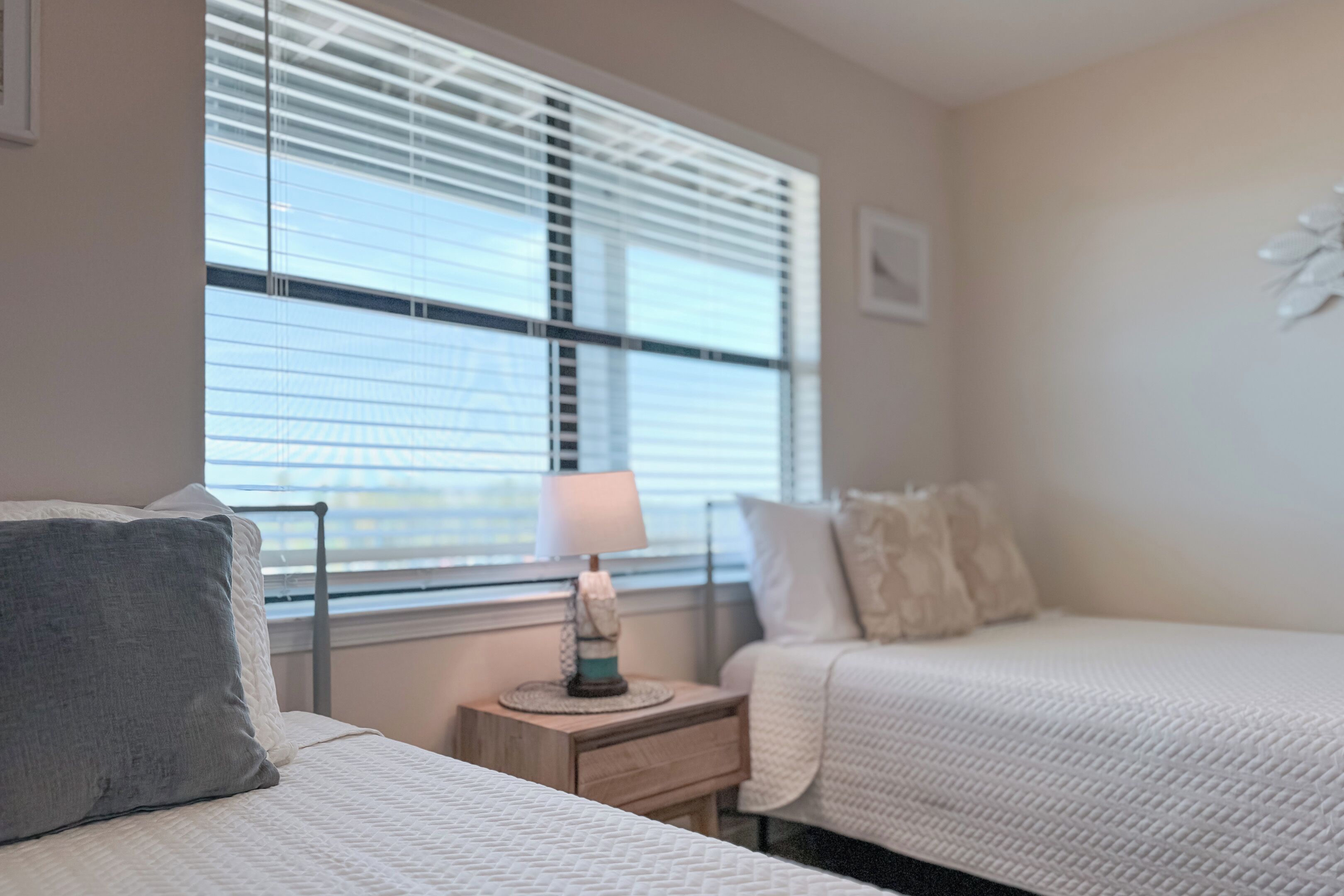 A bedroom with two beds, a bedside table with a lamp, and a window with blinds.
