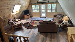 A cozy loft-style living room with wooden walls and floors, a large window, a sofa, a coffee table, and a TV. - Quiet mountain escape with great views. (Cimarron)