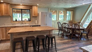 A kitchen with wooden cabinets, a large island with bar stools, a dining table with chairs, and large windows with a view of trees. - Quiet mountain escape with great views. (Cimarron)