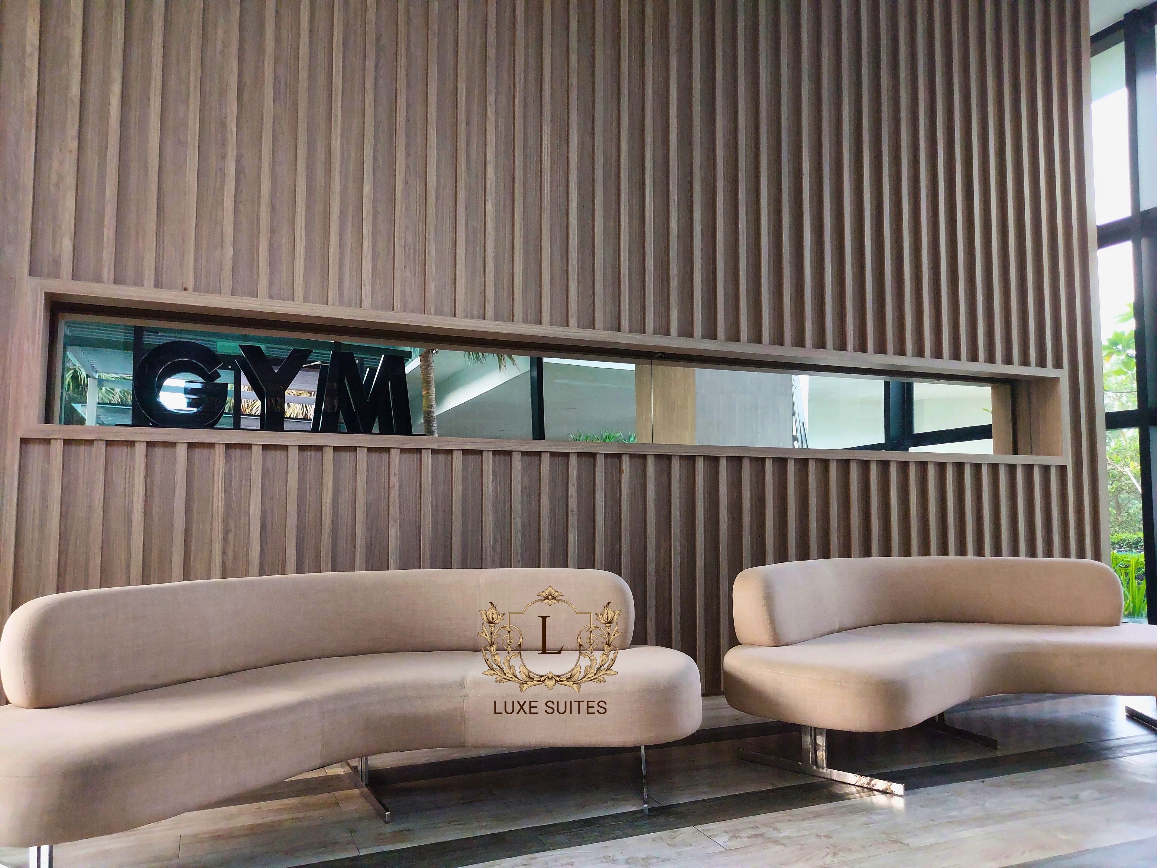 A modern interior with a wooden slatted wall, a large window, and two beige sofas labeled "LUXE SUITES".