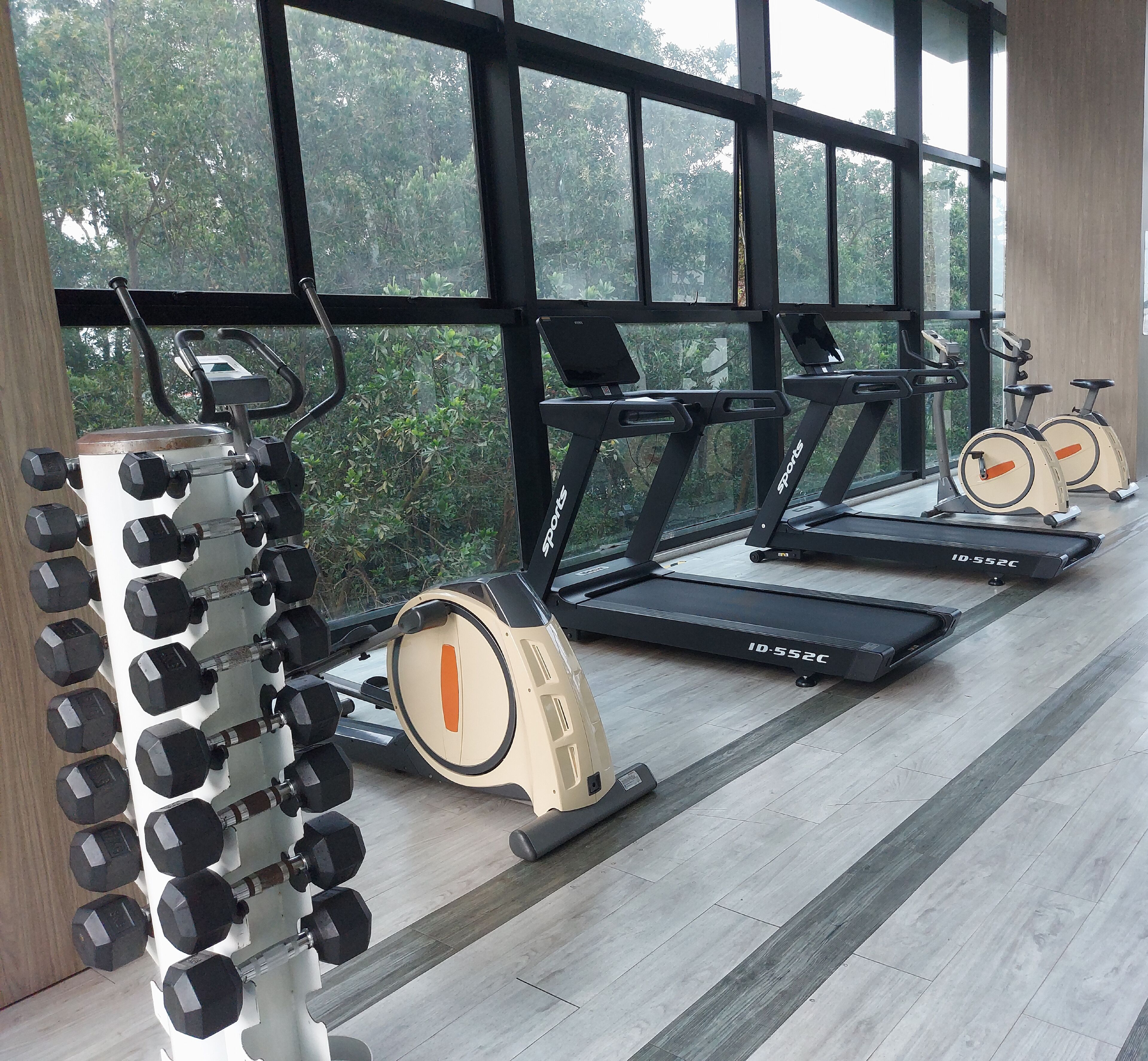 Un gimnasio con cintas de correr, un soporte para mancuernas y ventanas amplias con vistas a zonas verdes.