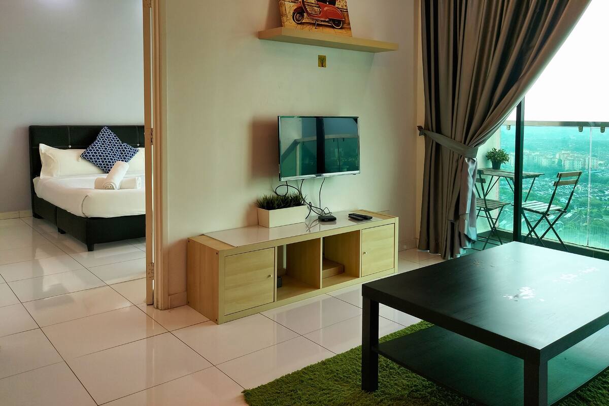 A modern living room with a flat-screen TV, a sofa, a coffee table, and a balcony with a city view.