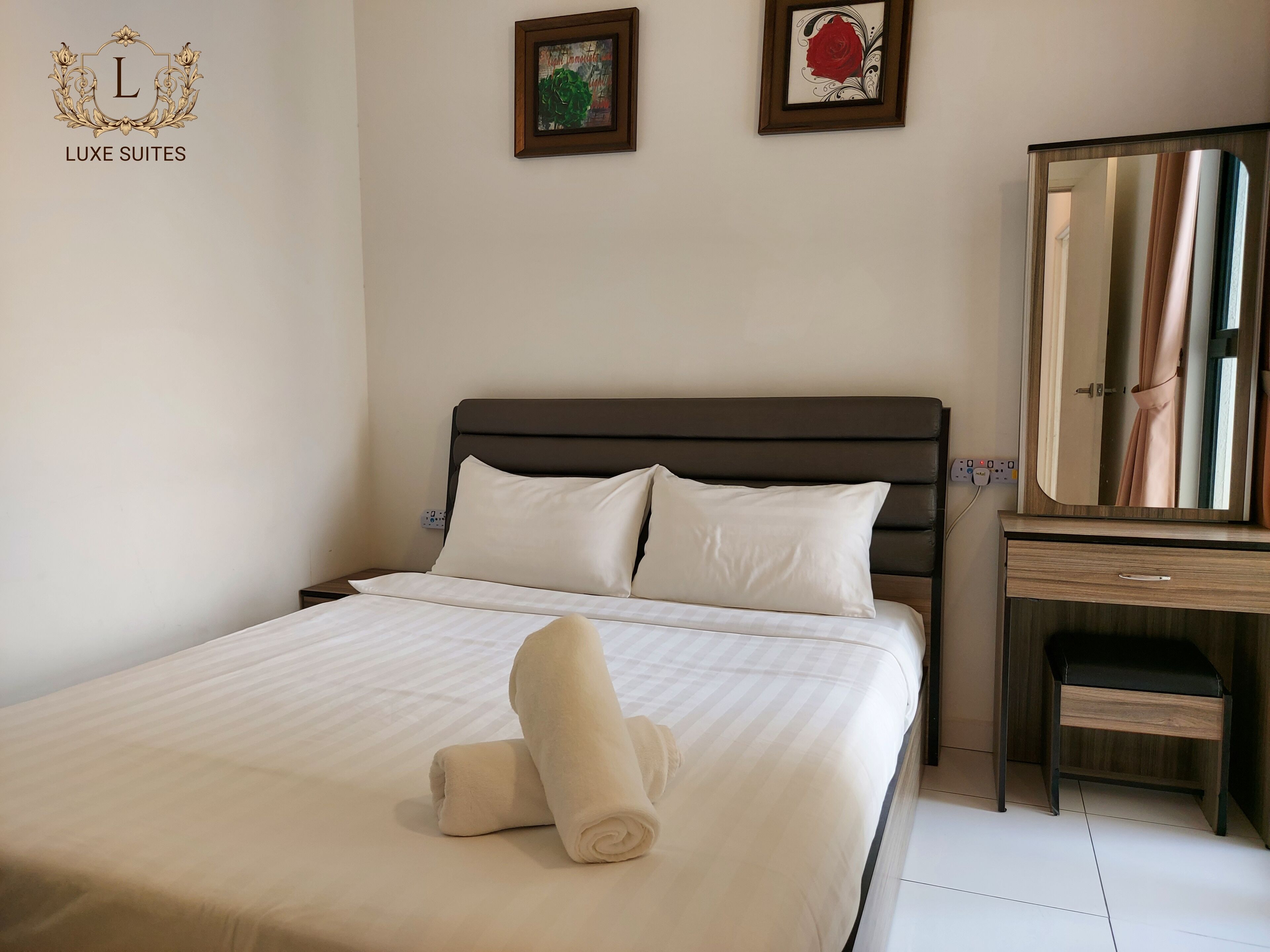 A neatly made bed with white linens and two pillows, a wooden nightstand with a mirror, and two framed pictures on the wall.