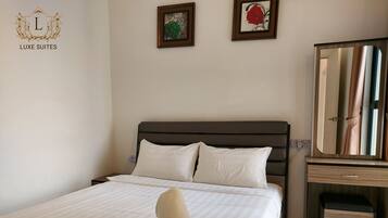 A neatly made bed with white linens and two pillows, a wooden nightstand with a mirror, and two framed pictures on the wall.