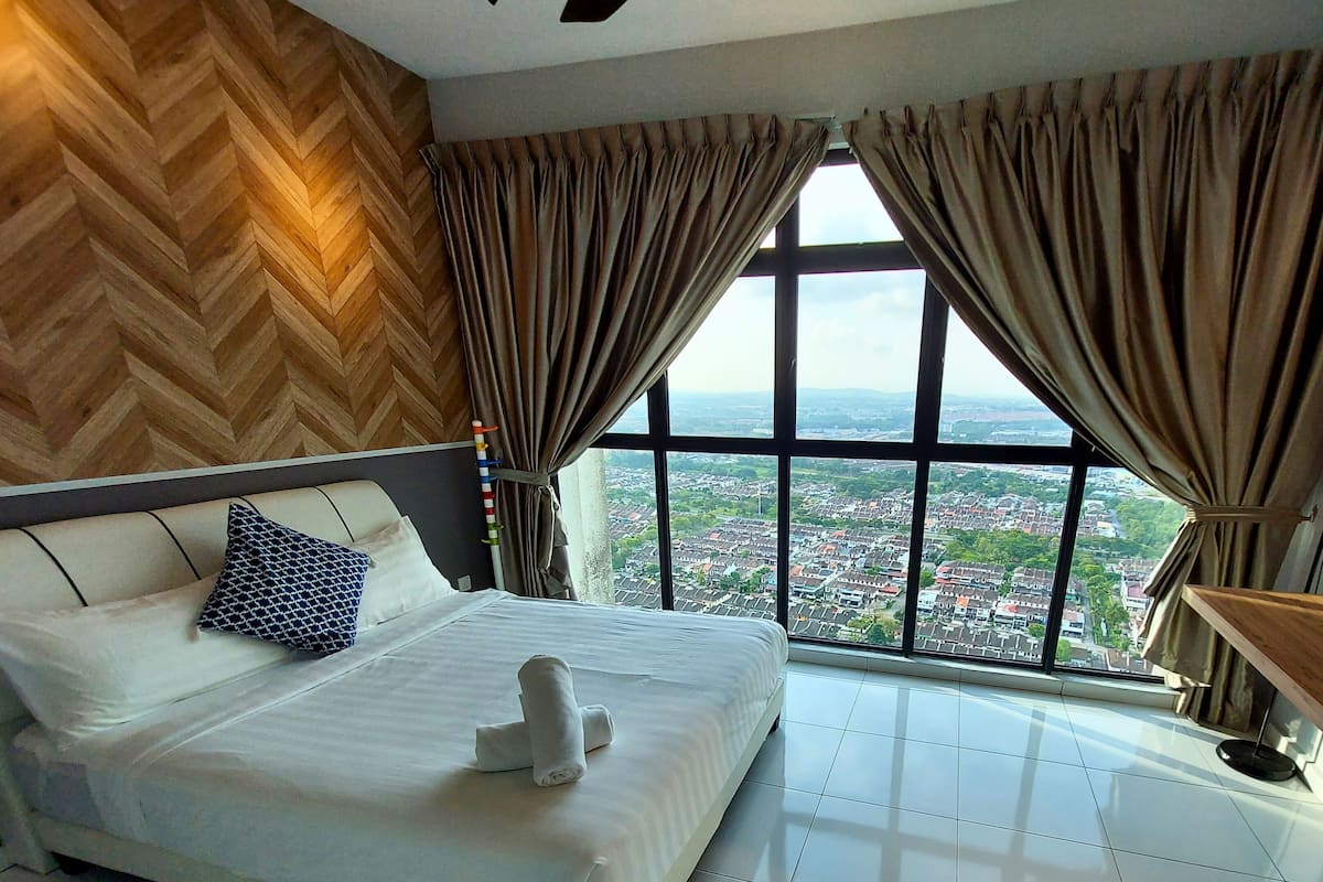 A bedroom with a large window, a bed with white linens, and a view of a cityscape.