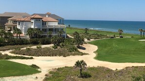 A golf course with a large house and ocean view.