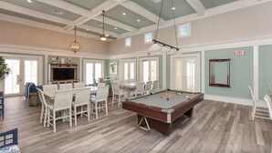 A spacious room with a pool table, white chairs, a television, and a dining area.