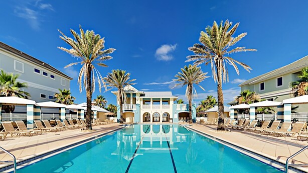 A swimming pool with lounge chairs and palm trees, surrounded by buildings with balconies.