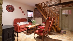 A cozy living room with a red sofa, a wooden coffee table, and a fireplace. There's a staircase with a wooden railing leading to a loft area.