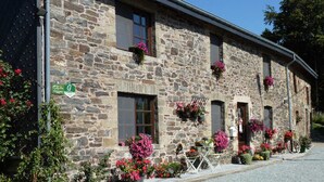 A stone building with multiple windows, some with flower boxes. There are signs indicating a parking area and a guesthouse.