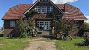 A two-story house with a red-tiled roof, a front porch with steps, and a bicycle parked outside.