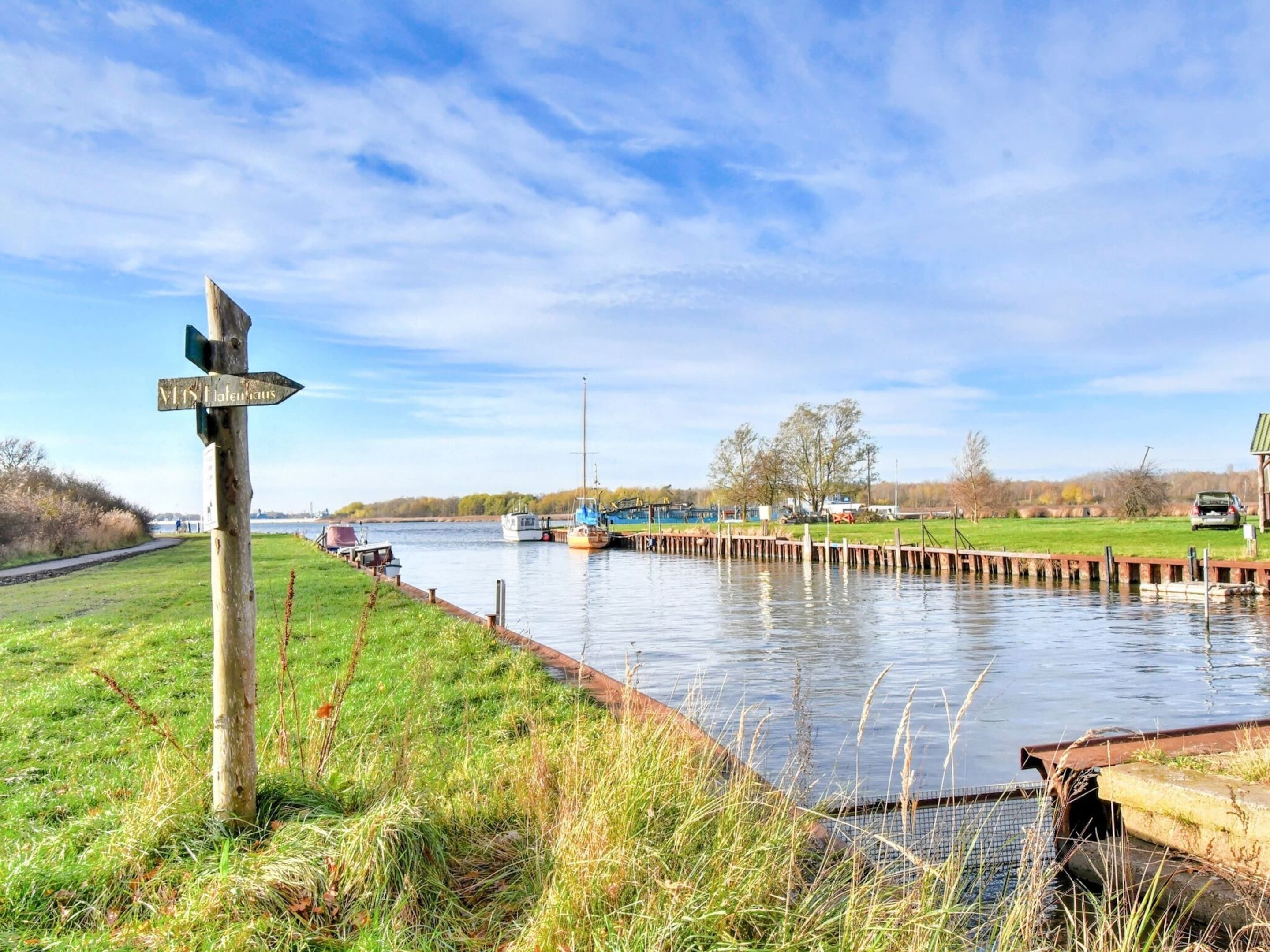 A canal with boats, a wooden signpost, and a grassy bank.
