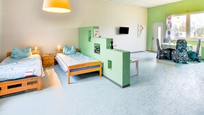 Una habitación con dos camas de madera, un escritorio verde, un televisor y una ventana con vistas.