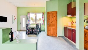 Una habitación con una mesa de comedor y sillas, una zona de cocina con armarios y un televisor montado en la pared.