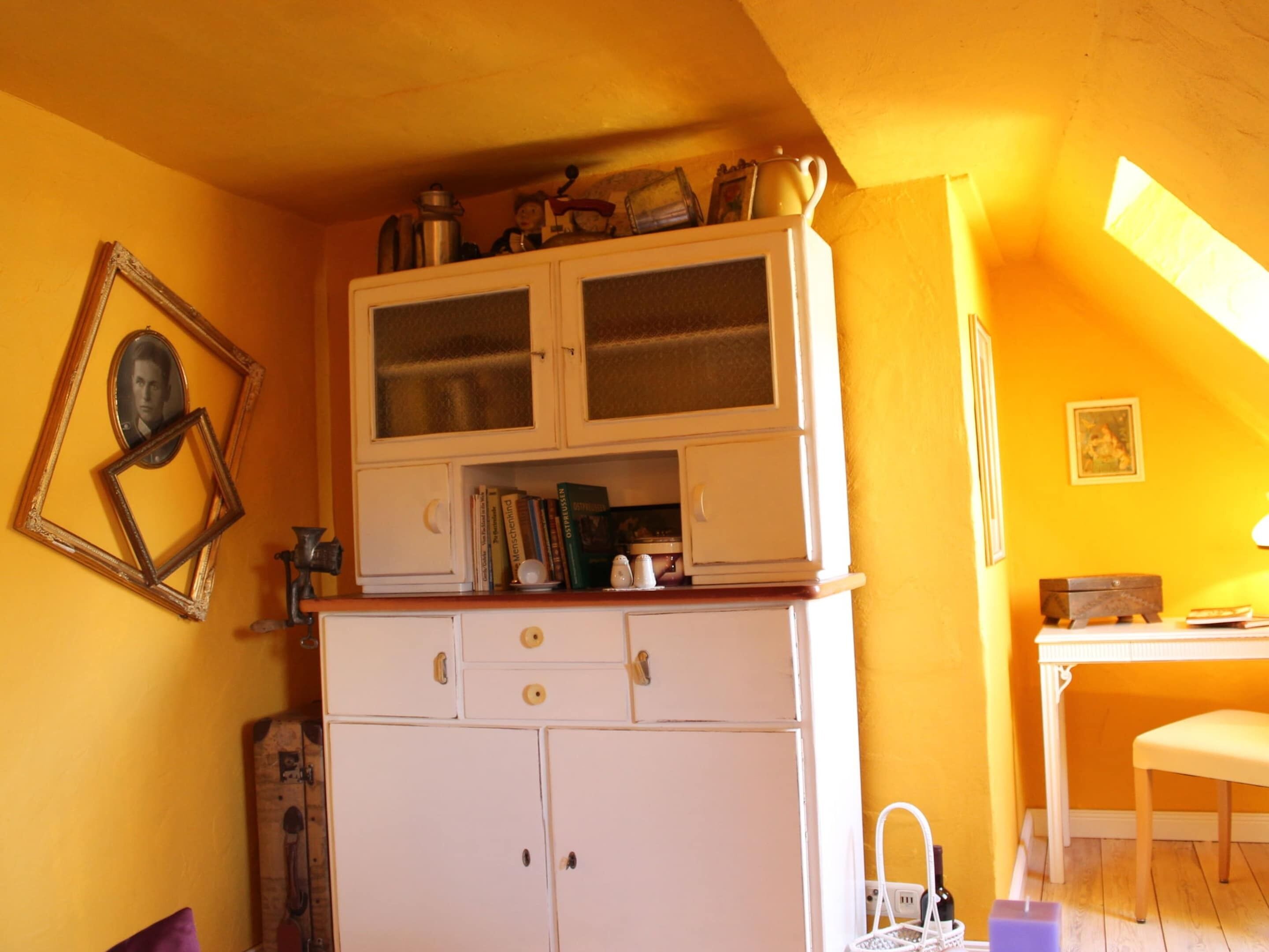 Une cuisine compacte avec des meubles blancs, un plan de travail en bois et un coin repas comprenant une table et une chaise blanches.