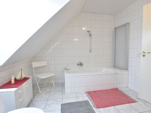 A modern bathroom with a sloped ceiling, a bathtub, a shower, a white chair, and a red rug. - Apartment in Wittenbeck With Terrace (Wittenbeck)