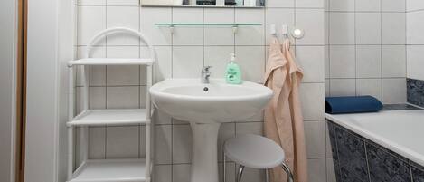 A bathroom with a white sink, a glass shelf, a white chair, a bathtub, and a mirror.