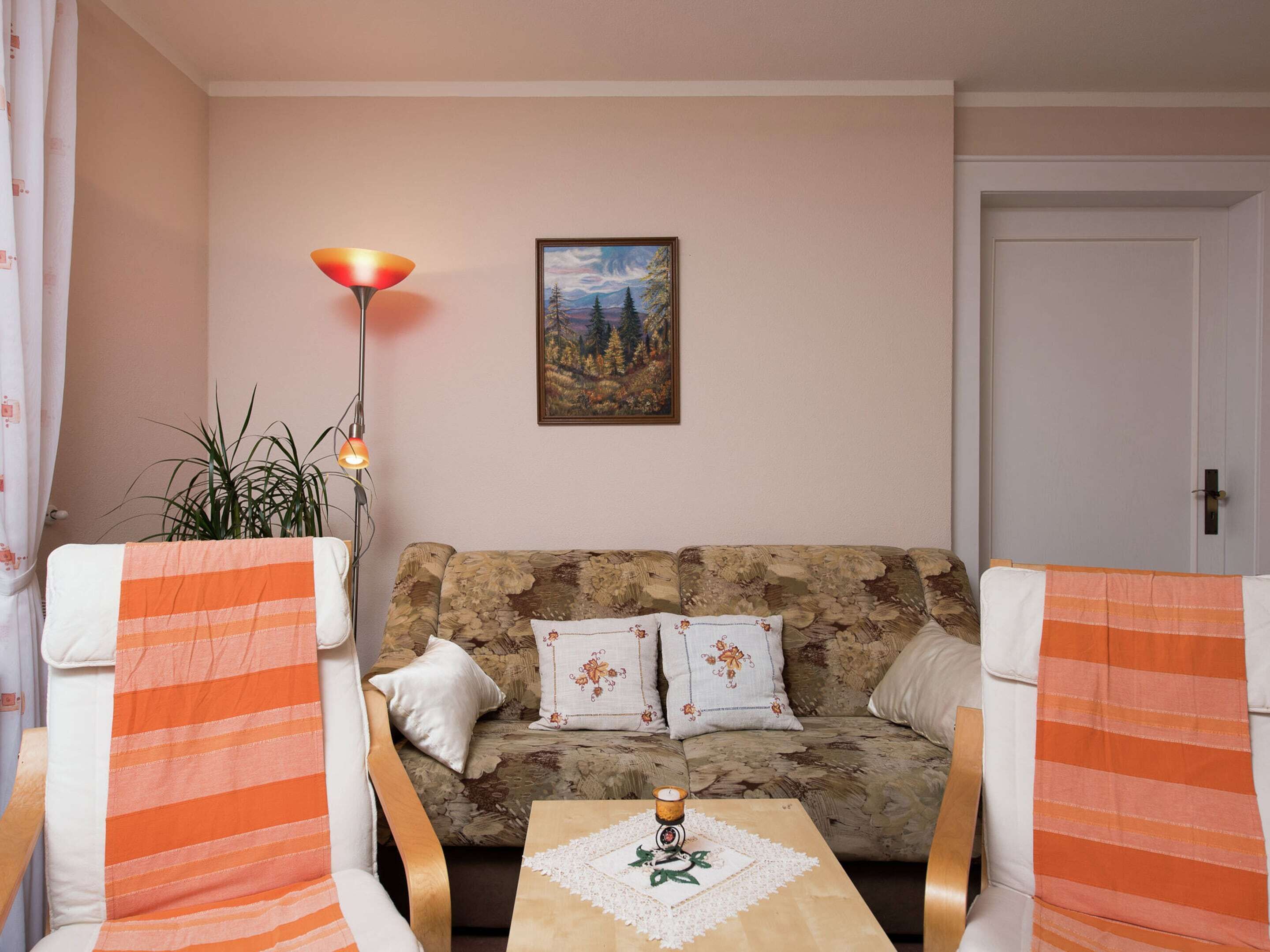 A living room with a sofa, two striped armchairs, a floor lamp, a painting, and a small table with a candle.