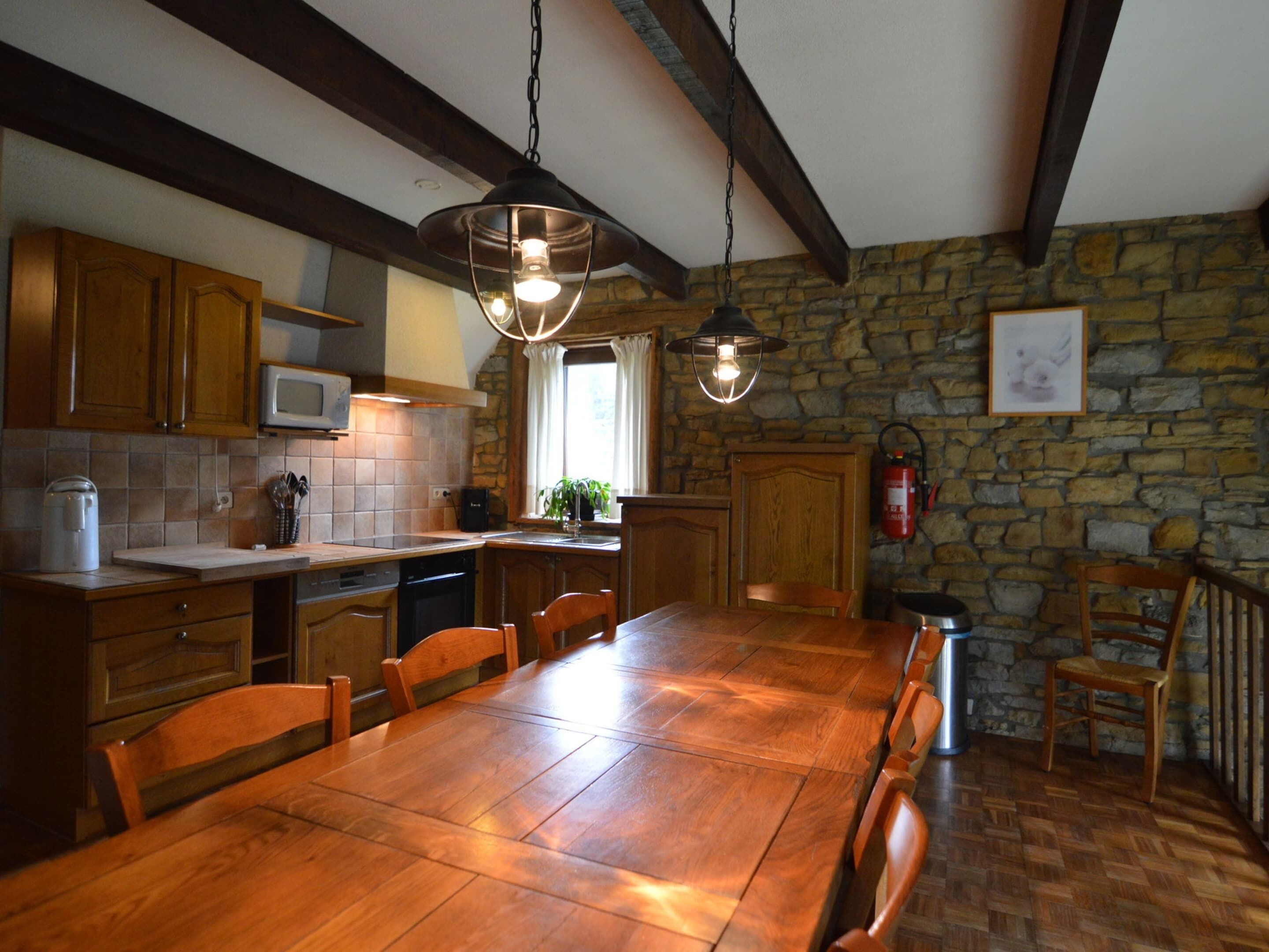 A rustic kitchen with wooden cabinets, a stone wall, and a large wooden dining table.