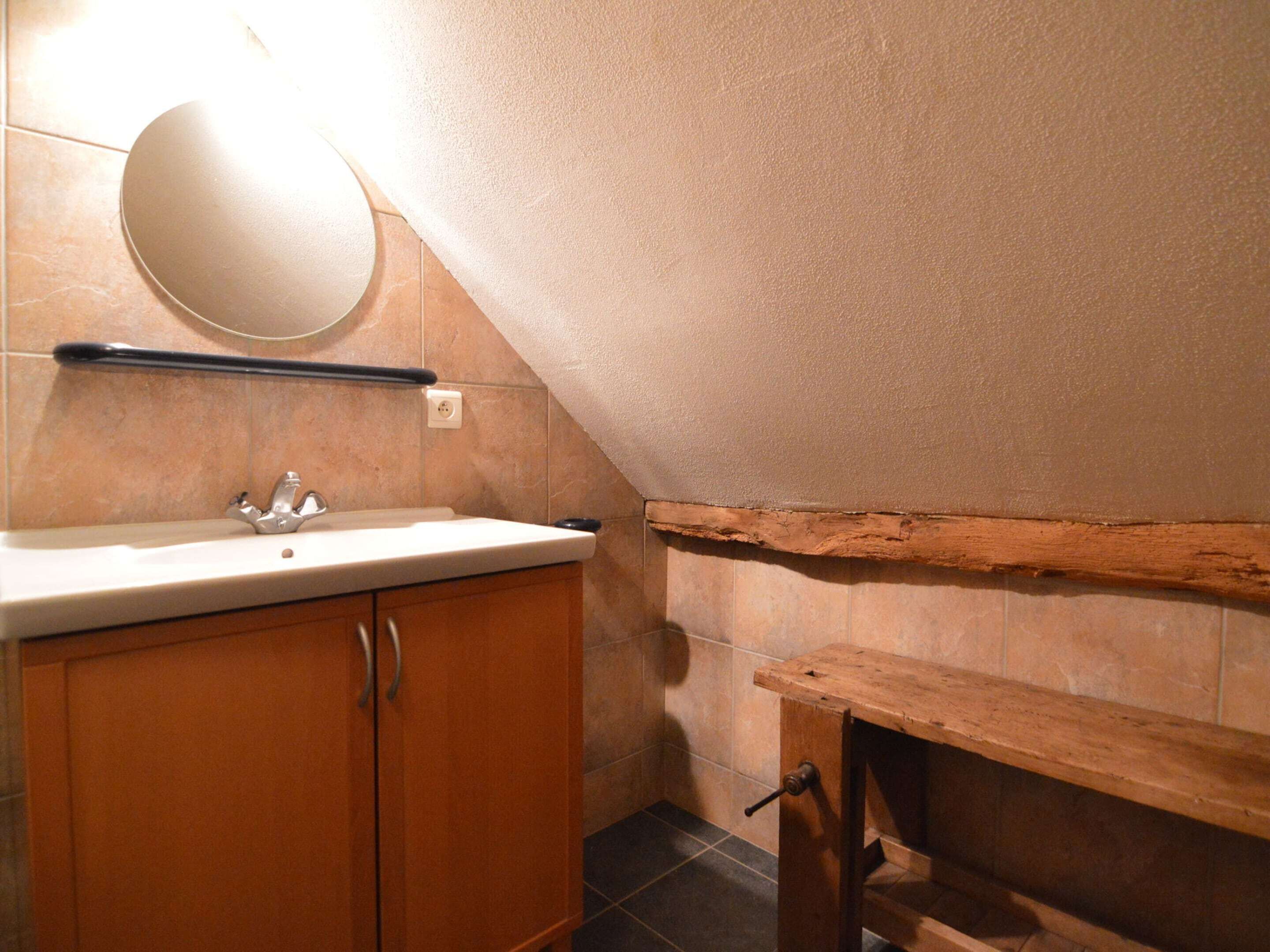 A bathroom with a sink, mirror, wooden cabinets, and a wooden bench.