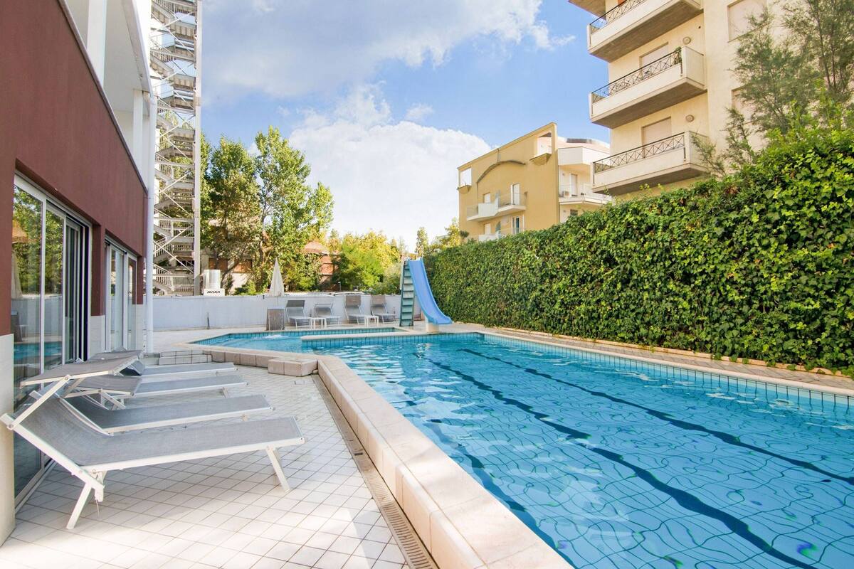 A swimming pool with lounge chairs, a slide, and a hedge.