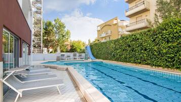 A swimming pool with lounge chairs, a slide, and a hedge.
