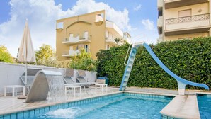 A swimming pool with a water slide, lounge chairs, and a small table. - Coastal Retreat in Riccione (Riccione)