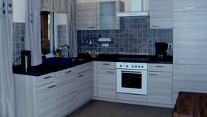 A modern kitchen with light wood cabinets, a black countertop, a built-in oven, and a coffee maker. - Bungalow Borgerende Nahe Strand & Reiten (Boergerende-Rethwisch)
