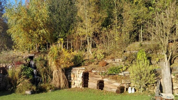 A garden with a stone wall, a small waterfall, and various plants. - Luxury Chalet in Stupna near Ski Area (Vidochov)
