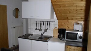 A compact kitchen with white cabinets, a built-in stove, a sink, and a microwave. - Charmantes Apartment in Jennewitz, in Ostseenahe (Kroepelin)