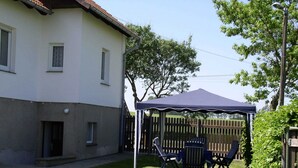 A covered patio area with outdoor furniture, a wooden fence, and a house in the background. - Charmantes Apartment in Jennewitz, in Ostseenahe (Kroepelin)