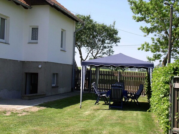 A covered patio area with outdoor furniture, a wooden fence, and a house in the background.