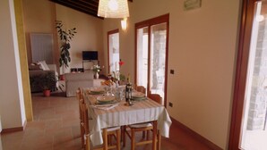 Un coin repas avec une table dressée pour quatre personnes, des chaises en bois, un luminaire suspendu et une vue à travers une porte vitrée.