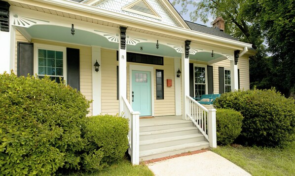 A two-story house with a porch, a front door, and a small staircase leading to the entrance.