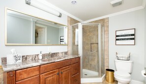 A bathroom with a marble vanity, a large mirror, a glass shower enclosure, and a framed inspirational quote on the wall.